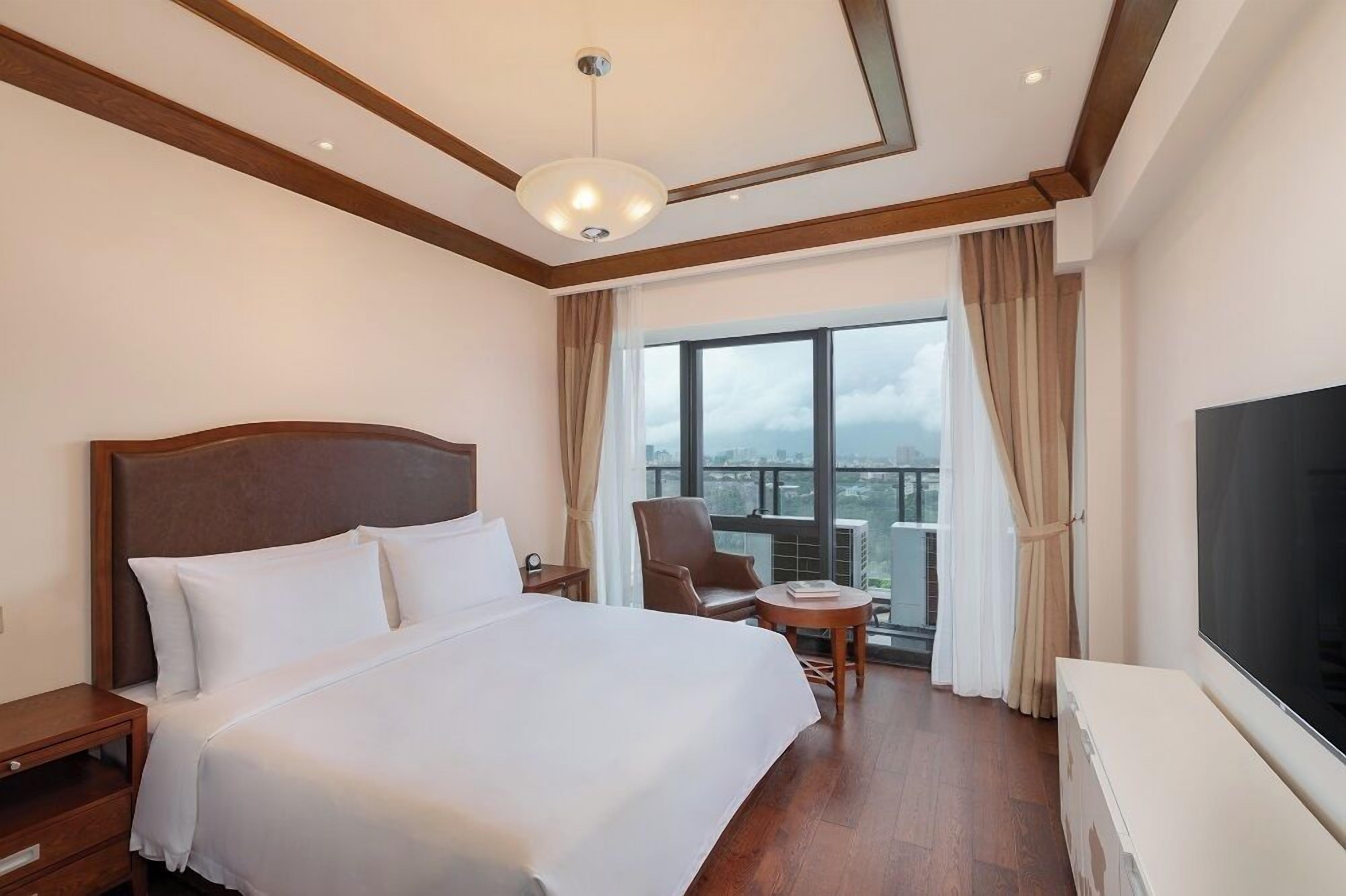 Una camera d'albergo con un letto grande, una televisione, una sedia, un tavolino e un balcone con vista.