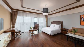 A hotel room with a bed, a desk, a chair, a sofa, a coffee table, and a painting on the wall.