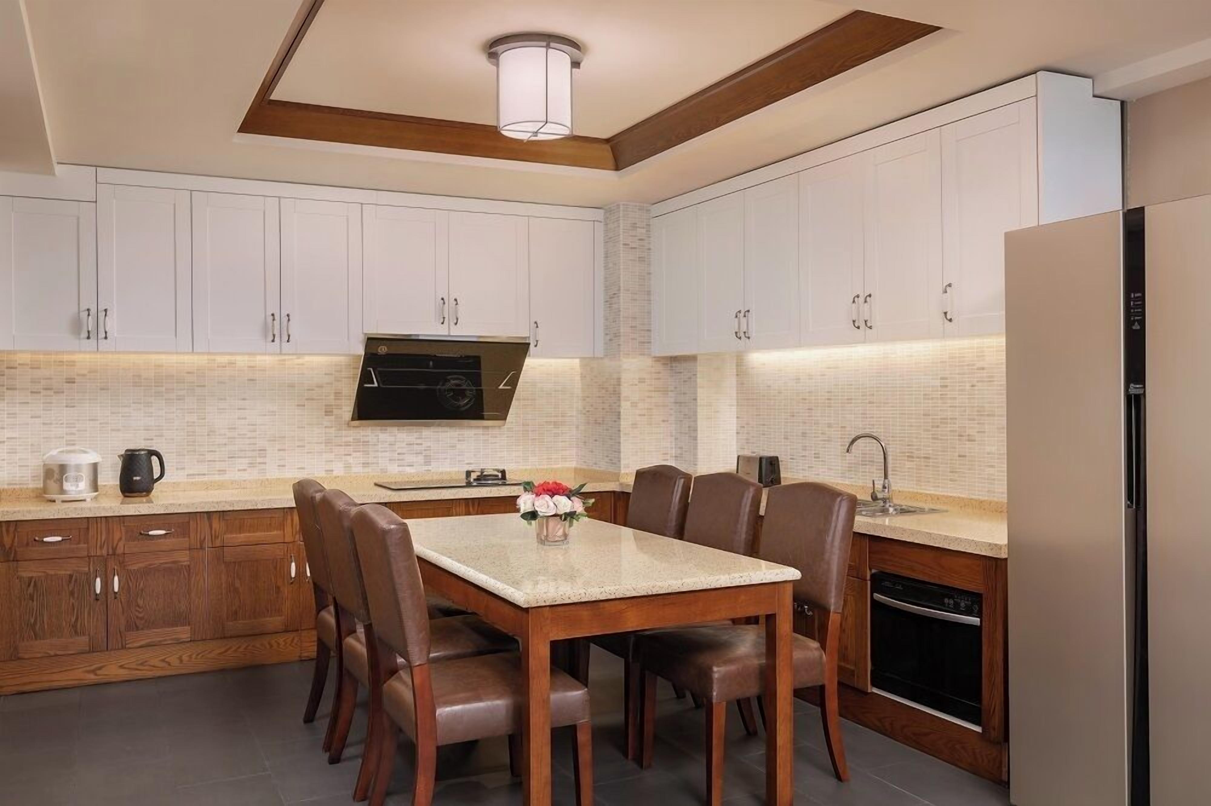 Una cocina moderna con armarios blancos, microondas integrado, una mesa de comedor con sillas y un refrigerador.