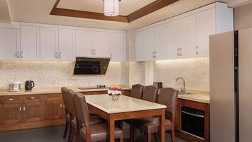 Una cocina moderna con armarios blancos, microondas integrado, una mesa de comedor con sillas y un refrigerador.