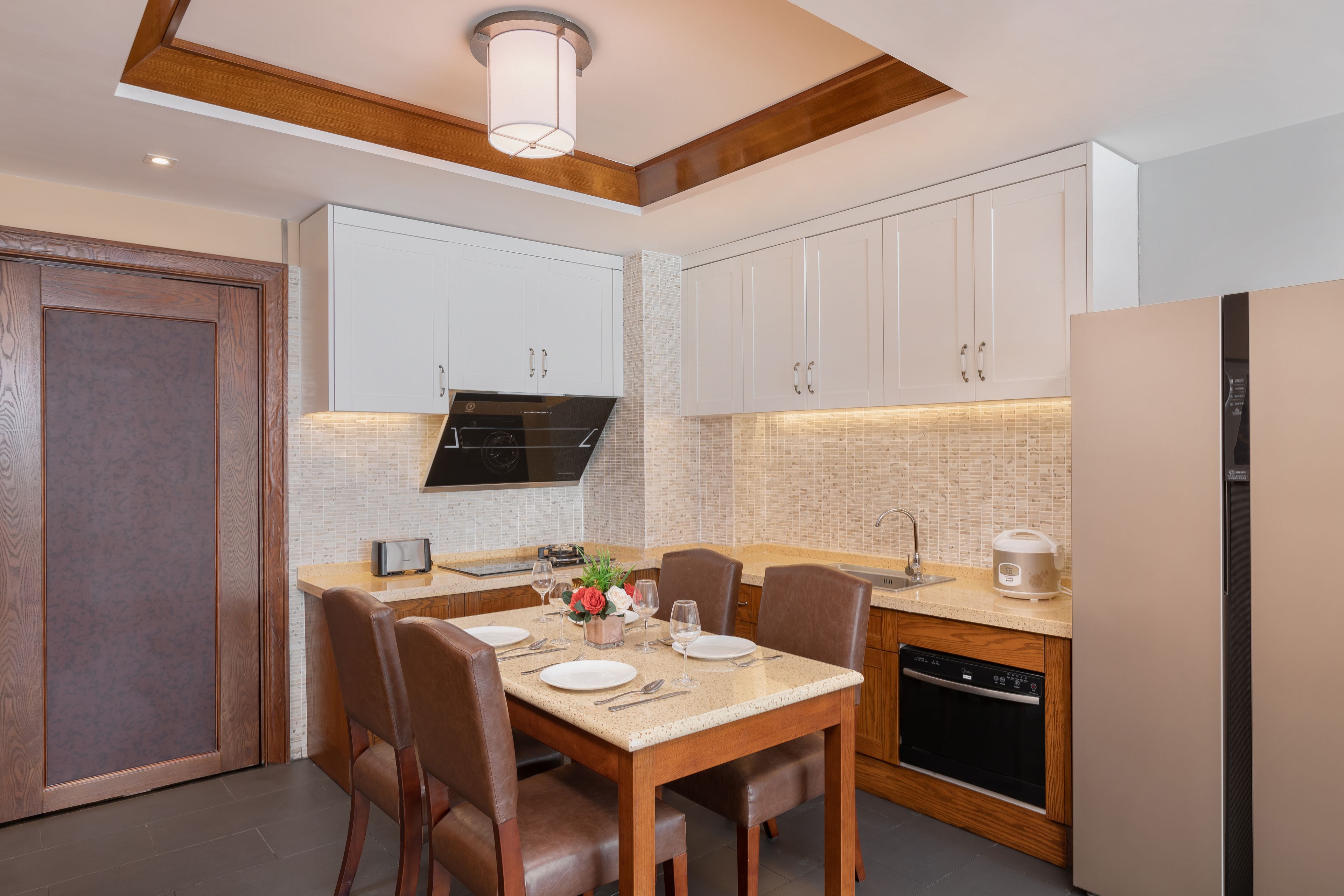 A modern kitchen with white cabinets, a wooden dining table, and a built-in oven.