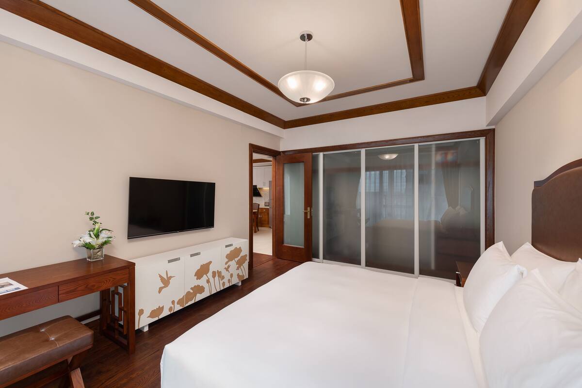 Une chambre d’hôtel dotée d’un grand lit, d’un téléviseur à écran plat, d’un bureau en bois et d’une porte-fenêtre coulissante donnant sur un balcon.