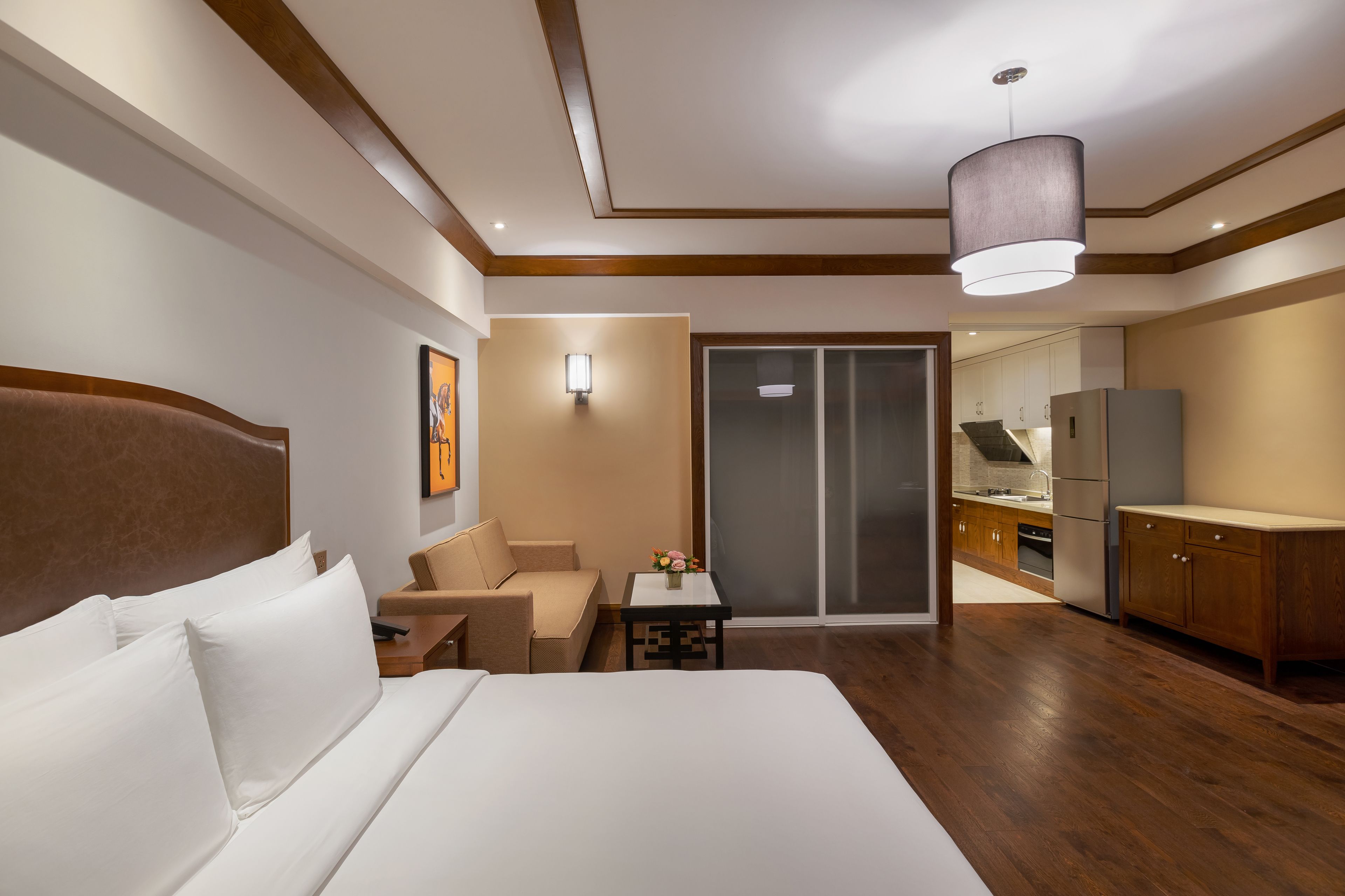 Een hotelkamer met een groot bed, een bank, een kleine tafel met een vaas, een keuken met kastjes en apparatuur, en een schuifdeurkast.