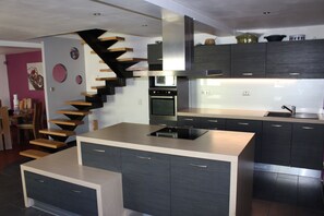 A modern kitchen with a central island, dark cabinetry, and a unique black and white spiral staircase. - House / villa complete with swimming pool 5 minutes from Colmar (Ingersheim)