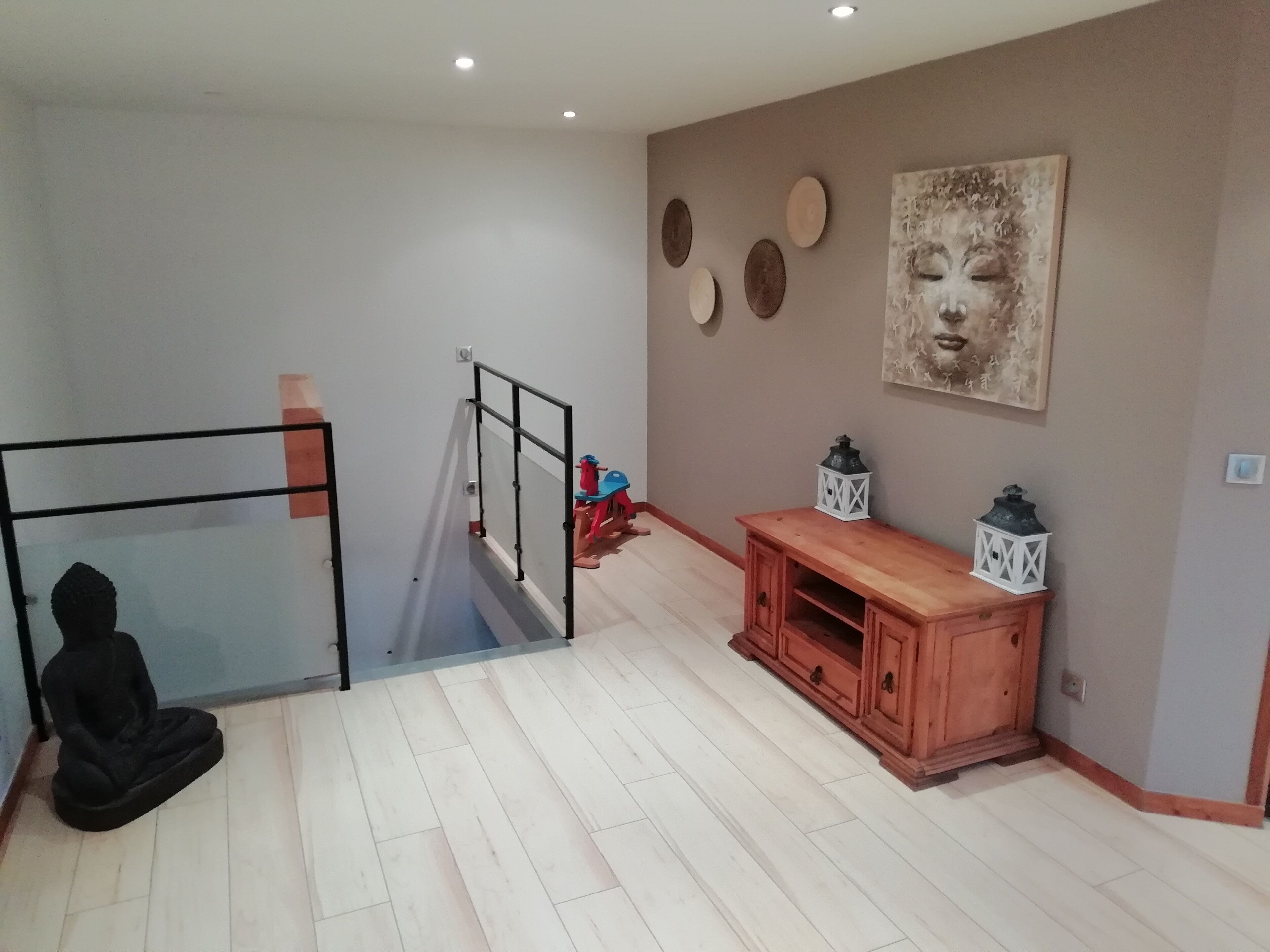 A spacious room with a wooden cabinet, a meditation mat, and a staircase.