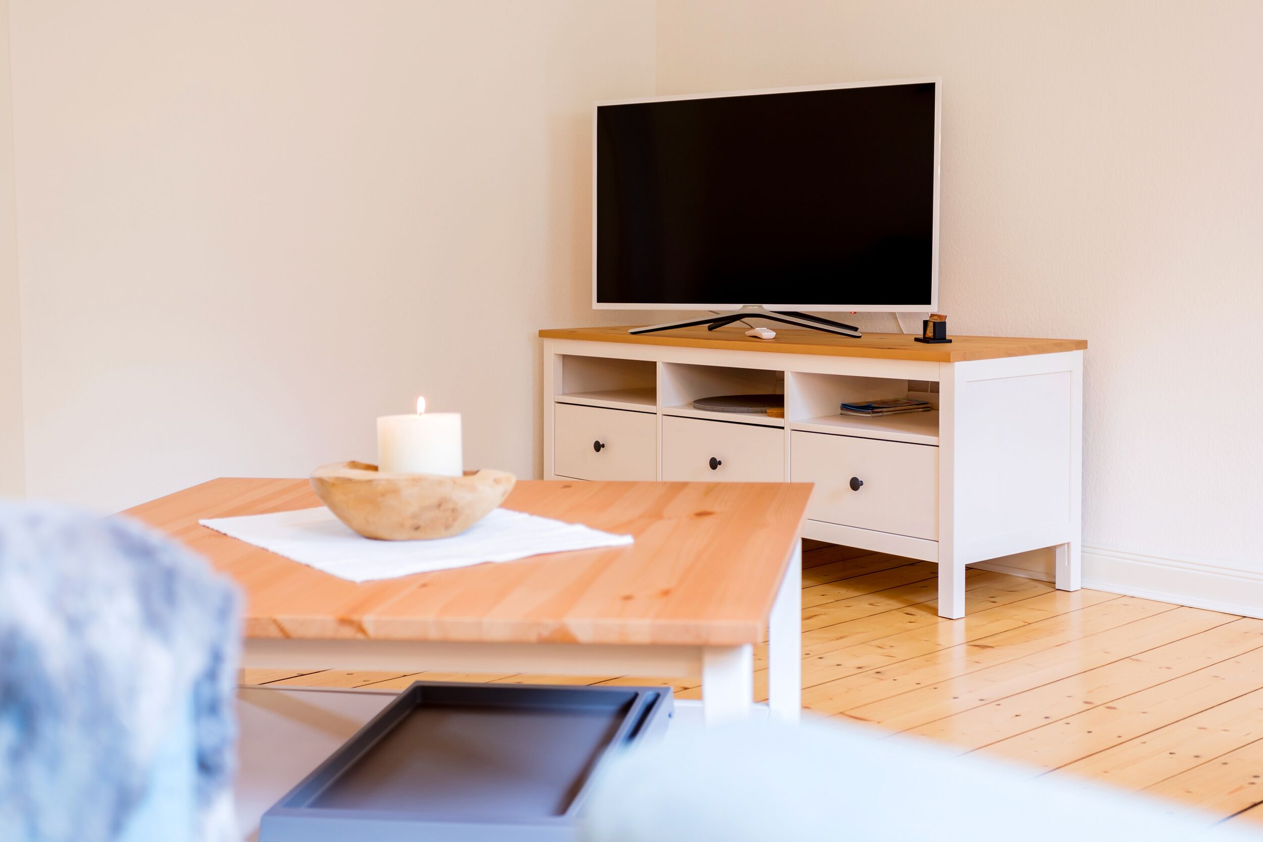 Ein modernes Wohnzimmer mit einem Holztisch, einem weißen Schrank und einem Flachbildfernseher.