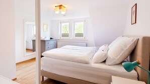 Ein Schlafzimmer mit Bett, Nachttisch, Lampe und einem Fenster mit Blick auf Grünflächen.
