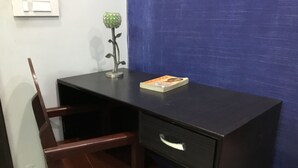Un pequeño escritorio de madera oscura con un cajón, una silla y un objeto decorativo verde sobre la superficie.