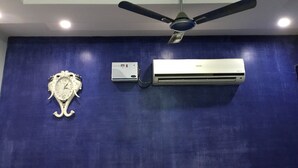 Una habitación con pared azul, ventilador de techo, aire acondicionado y un reloj decorativo.