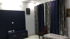 Una habitación con un armario azul oscuro, una mesita con mantel blanco, un tapete floral y cortinas estampadas.