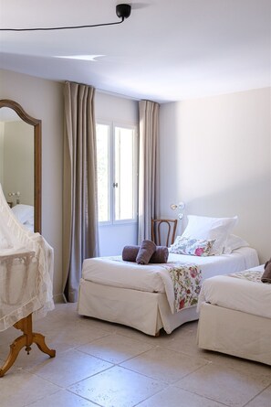 Two single beds with white linens and a floral-patterned throw blanket, a wooden chair, and a large mirror.