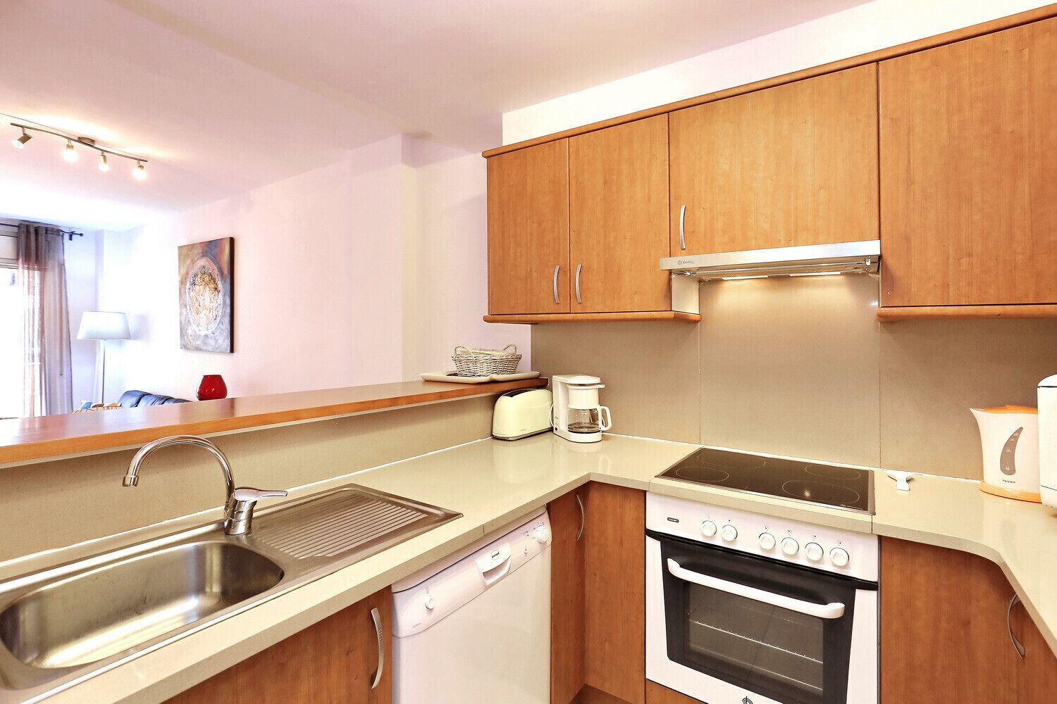 A modern kitchen with wooden cabinets, a stainless steel sink, a dishwasher, a stove, and a coffee maker.