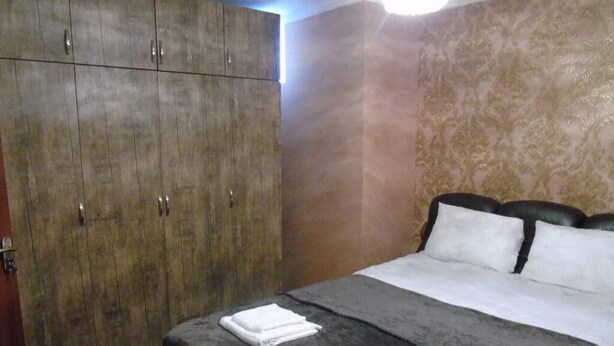 Ein Schlafzimmer mit großem Kleiderschrank, einem Bett mit weißer und grauer Bettwäsche und einer Wand mit Muster.