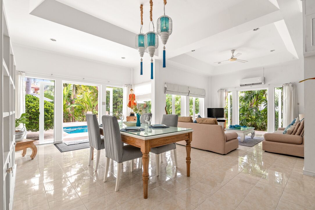 A spacious living area with a glass dining table, beige sofas, and a TV.