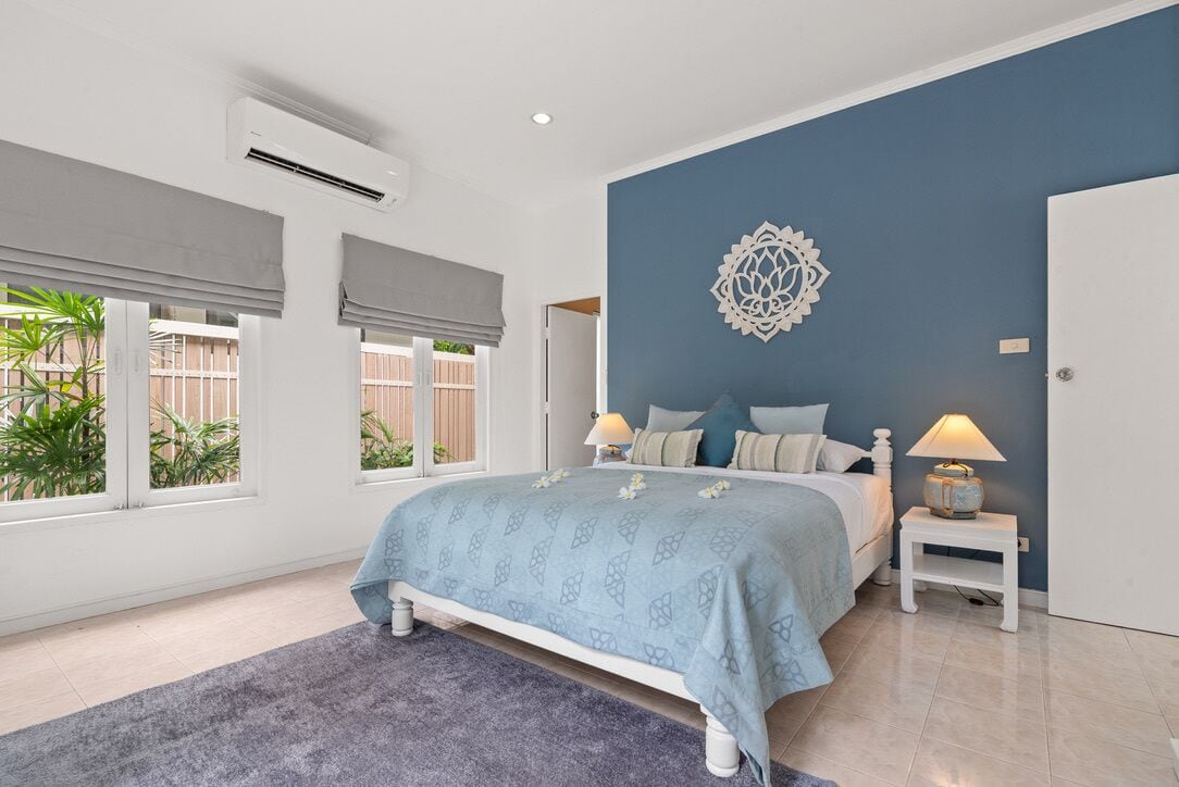 A bedroom with a bed, two bedside tables, a decorative wall piece, and large windows with blinds.