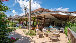 An outdoor patio area with wicker furniture, a covered seating area, and a view of the surrounding garden. - Baan Chanchai (Koh Samui)