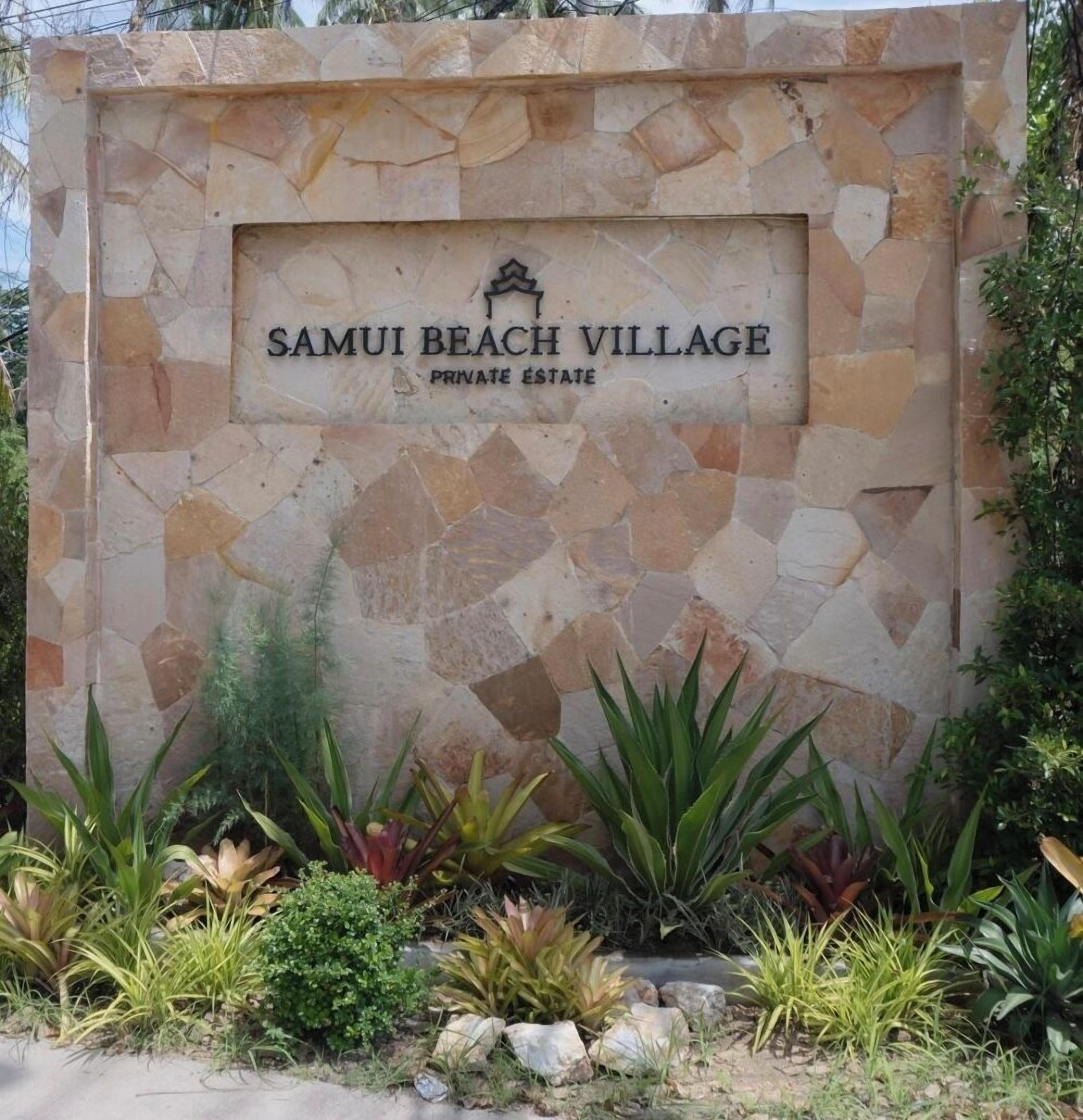 A stone wall with the text "SAMUI BEACH VILLAGE PRIVATE ESTATE" and a logo above it.