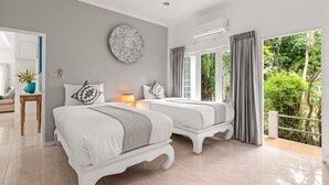 A bedroom with two beds, a large circular wall decoration, and a view of greenery outside. - Baan Chanchai (Koh Samui)