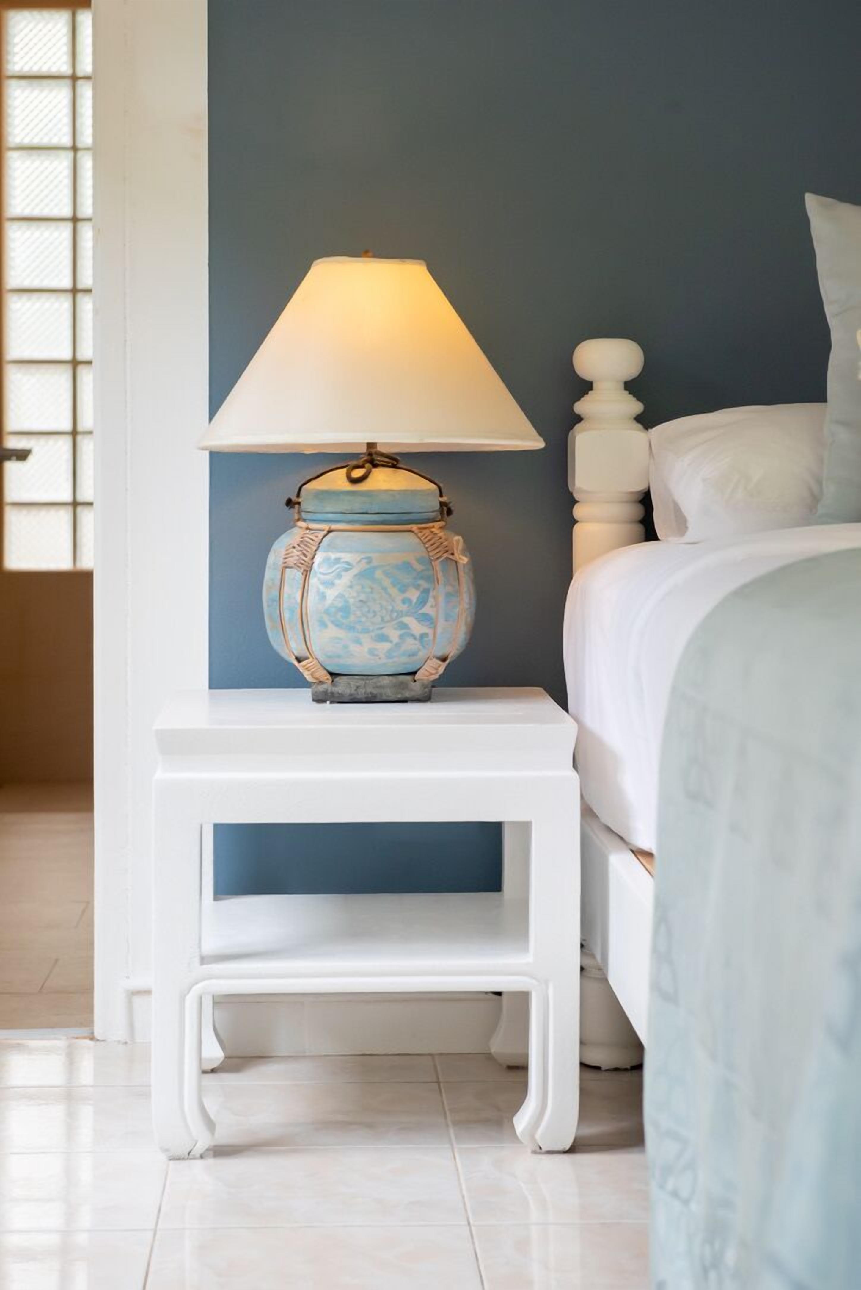 A bedroom with a bed, a white nightstand with a lamp, and a blue wall.