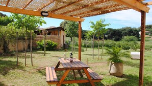 A wooden picnic table under a pergola in a grassy area with a house in the background.