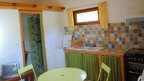 A compact kitchen with a tiled backsplash, a window with yellow curtains, a sink, and a stove.