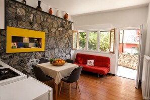 A kitchen with a stone wall, a dining table with chairs, a red sofa, and a window with a view of greenery. - Polly, few steps from the beach -Cinque Terre ,Monterosso. (Monterosso al Mare)