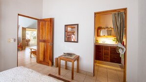 A room with a wooden door, a small table with a book, a mirror, and a bathroom with a sink and mirror. - Casa tropical - Located in Playa Guiones - Nosara - Costa Rica (Playa guiones)