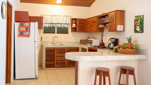 A kitchen with wooden cabinets, a refrigerator, a microwave, a sink, and a small bar area with stools. - Casa tropical - Located in Playa Guiones - Nosara - Costa Rica (Playa guiones)