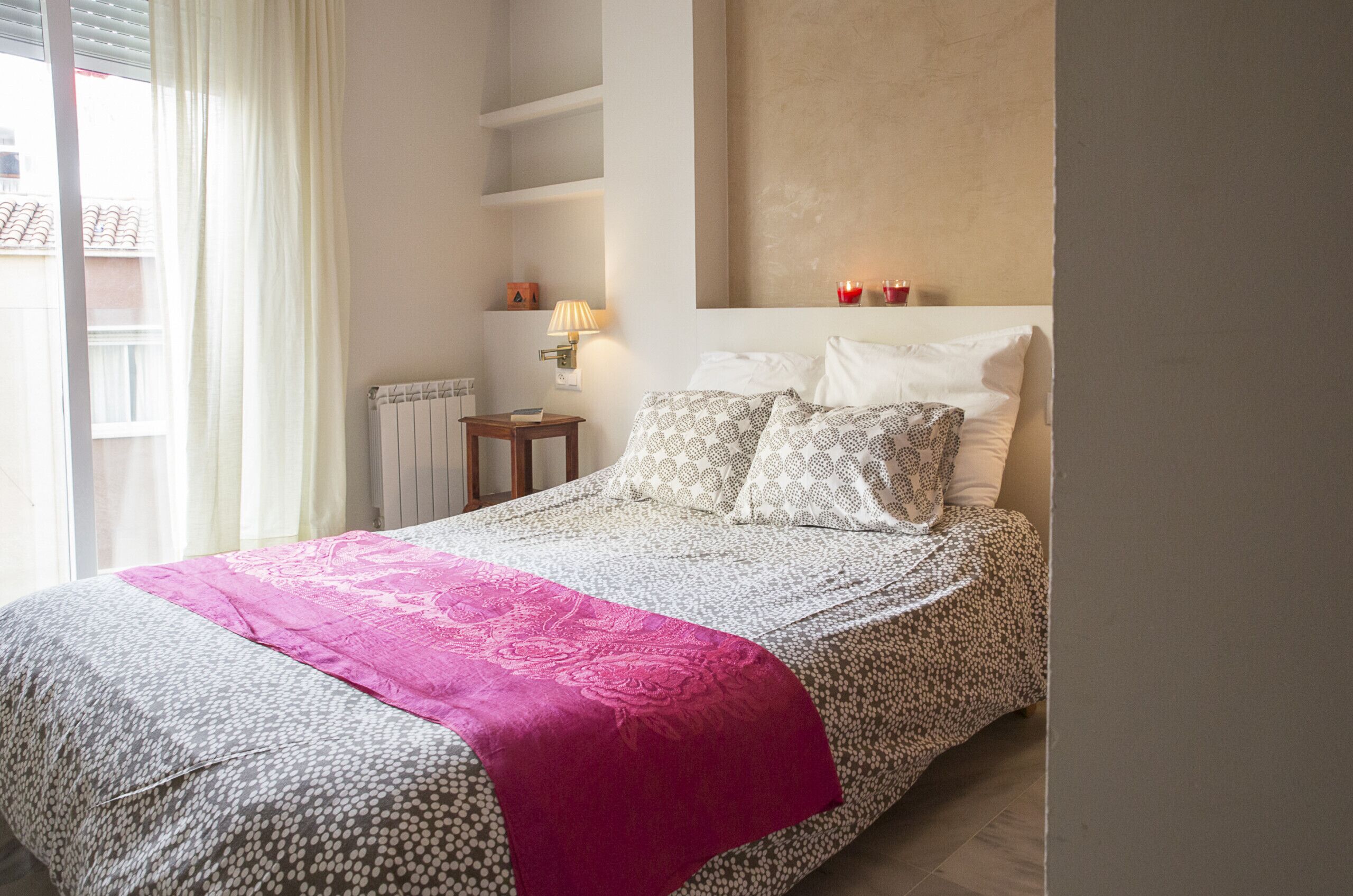 A bedroom with a bed, a nightstand, a lamp, and a window with curtains.