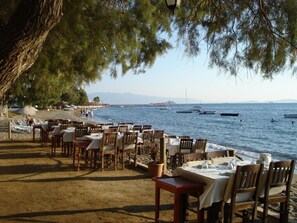 Ein Restaurant am Meer mit Außenbestuhlung, Blick auf das Meer und Booten in der Ferne.
