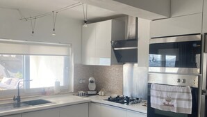 A modern kitchen with white cabinets, a built-in oven, and a window providing natural light. - Private Pool , Wifi,BBQ, sea views Bodrum kadikalesi Garden Apartment (Bodrum Kadikalesi)