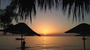A sunset view with two umbrellas and a person standing by the water. - Private Pool , Wifi,BBQ, sea views Bodrum kadikalesi Garden Apartment (Bodrum Kadikalesi)