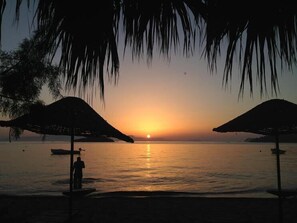A sunset view with two umbrellas and a person standing by the water.