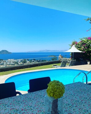 A pool with a view of the sea, a table with a floral tablecloth, and a vase with flowers. - Private Pool , Wifi,BBQ, sea views Bodrum kadikalesi Garden Apartment (Bodrum Kadikalesi)