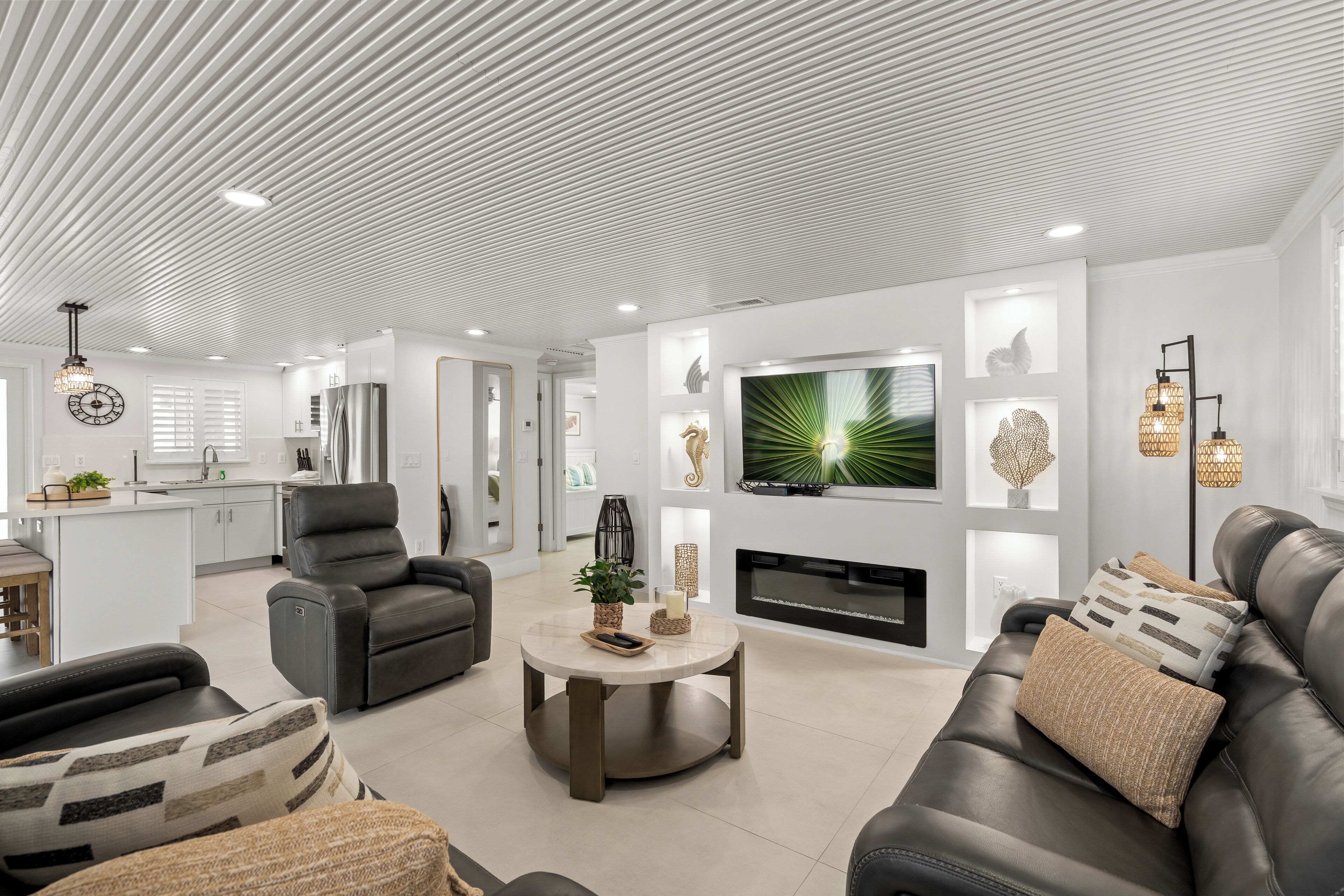 A modern living room with a fireplace, leather sofas, a round coffee table, and a TV mounted on the wall.