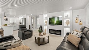 Ein modernes Wohnzimmer mit Kamin, Ledersofas, einem runden Couchtisch und einem an der Wand montierten Fernseher.