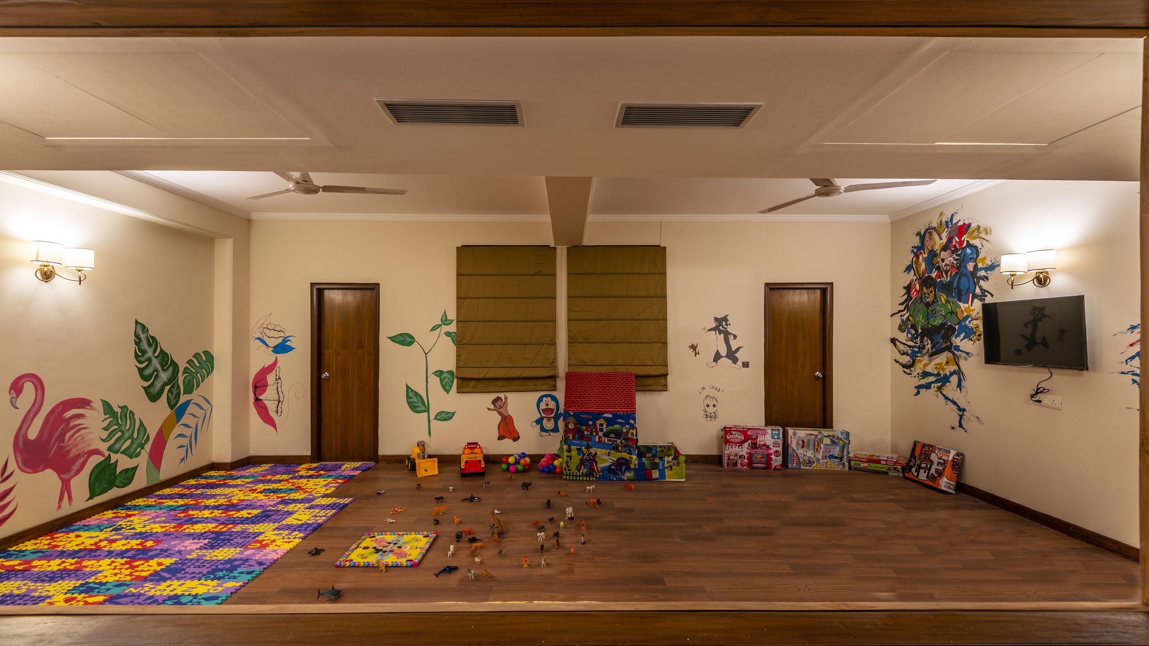 Een kamer met houten vloeren, twee deuren, plafondventilatoren, muurschilderingen en een televisie.