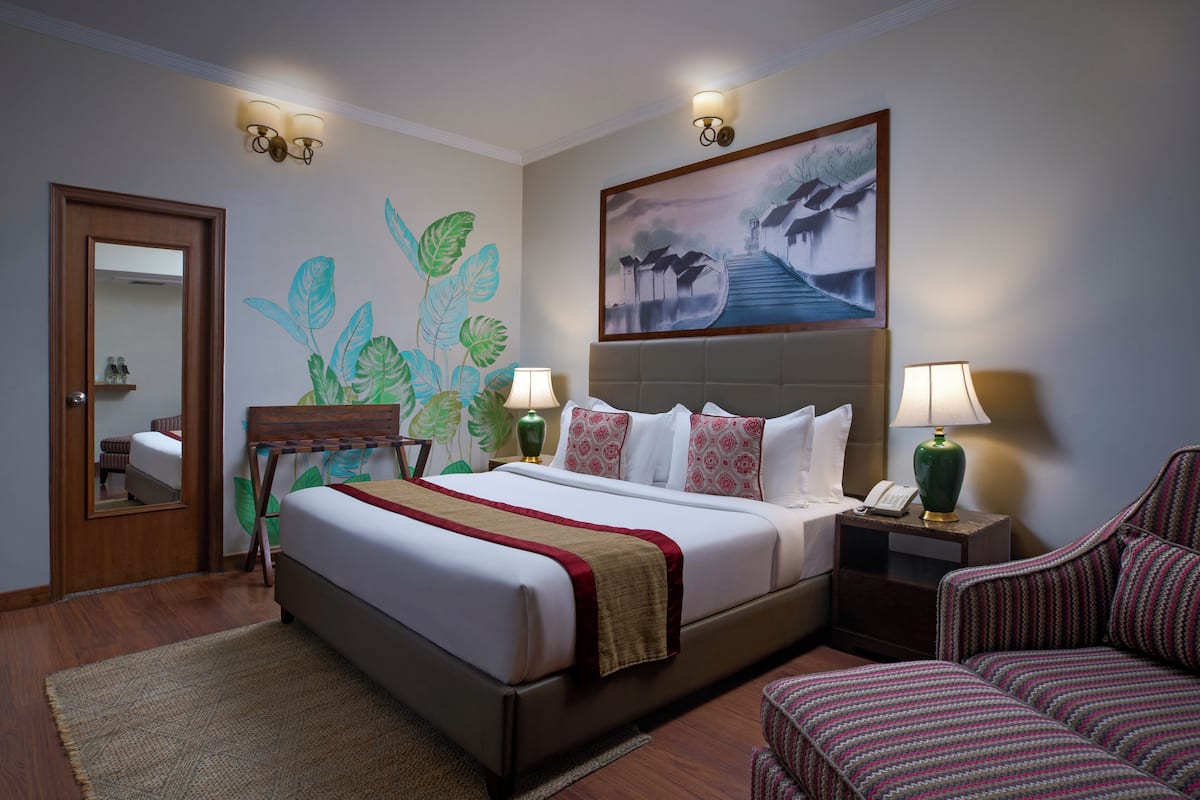 Une chambre d’hôtel avec un grand lit, deux tables de chevet avec des lampes, une chaise et un tableau au mur.