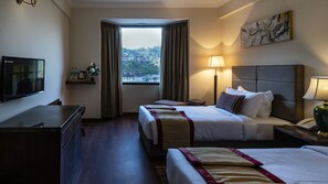 Habitación de hotel con dos camas, un escritorio, televisor, ventana con cortinas, lámpara y un cuadro en la pared.