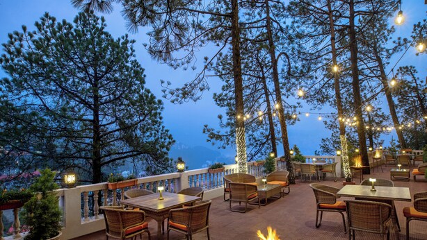 An outdoor patio area with wicker furniture, string lights, and a fire pit. - 8fold by LaRiSa, Shimla (Shimla)
