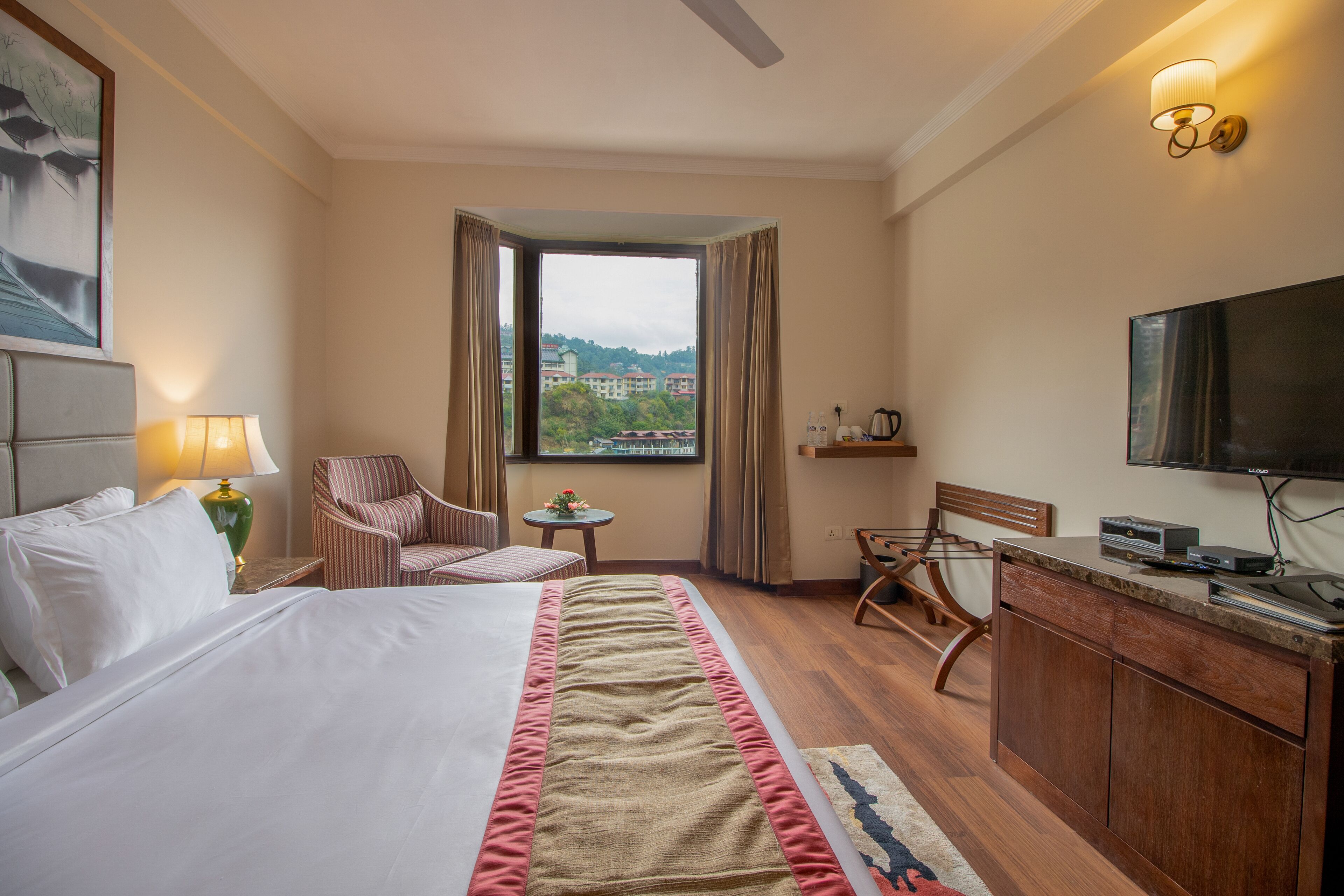 A hotel room with a bed, a desk, a chair, a television, and a window with a view of buildings.
