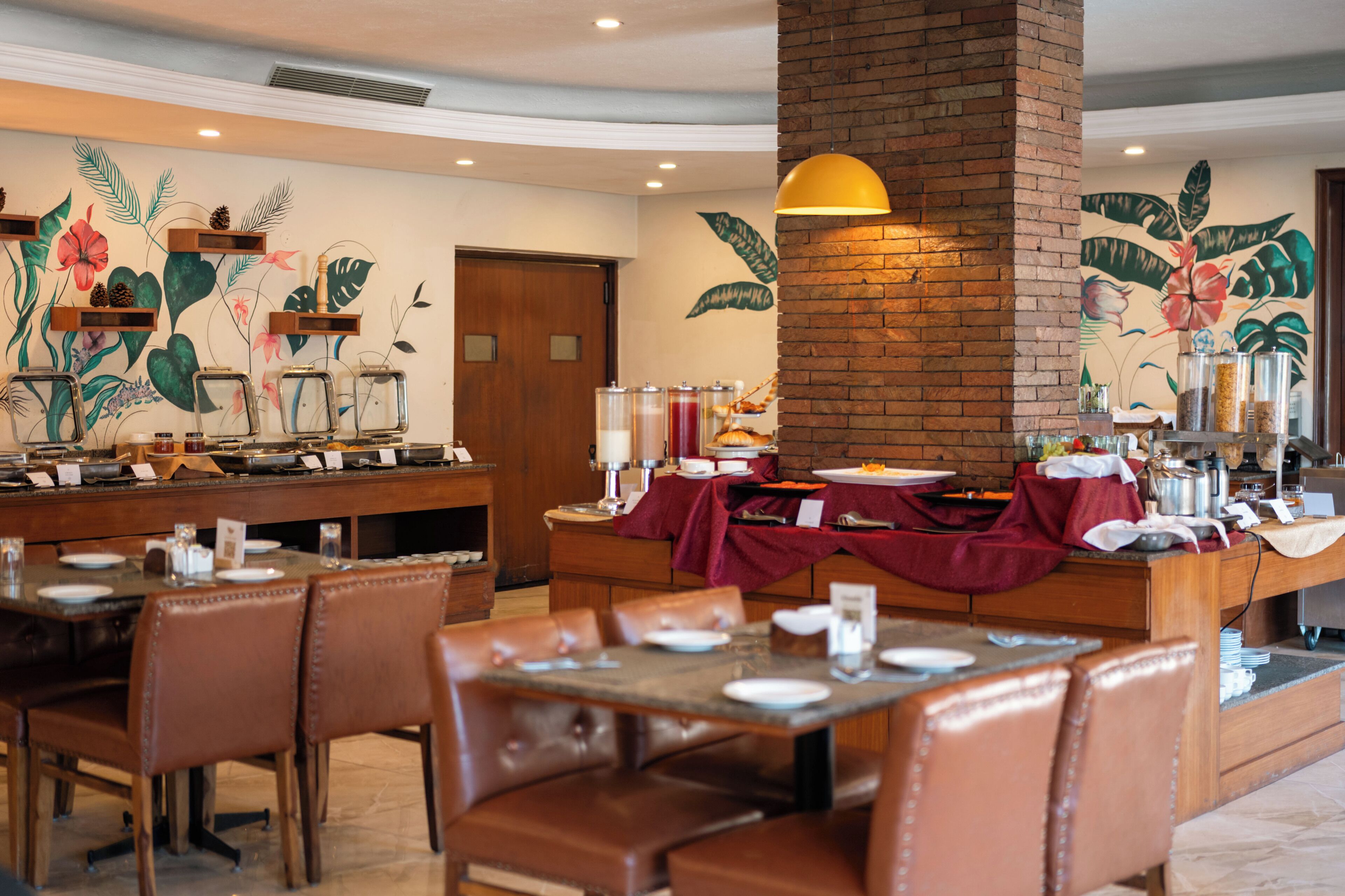 A restaurant with booths and tables, a brick column, and a mural of tropical flowers.
