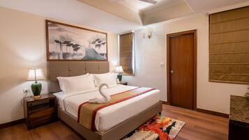 A hotel room with a bed, a nightstand with a lamp, a wall-mounted painting, a door, and a ceiling fan.