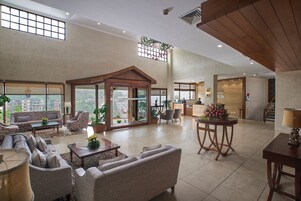 A spacious living area with a sofa set, a coffee table, and a dining table with chairs. There is a large window with a view of buildings outside.