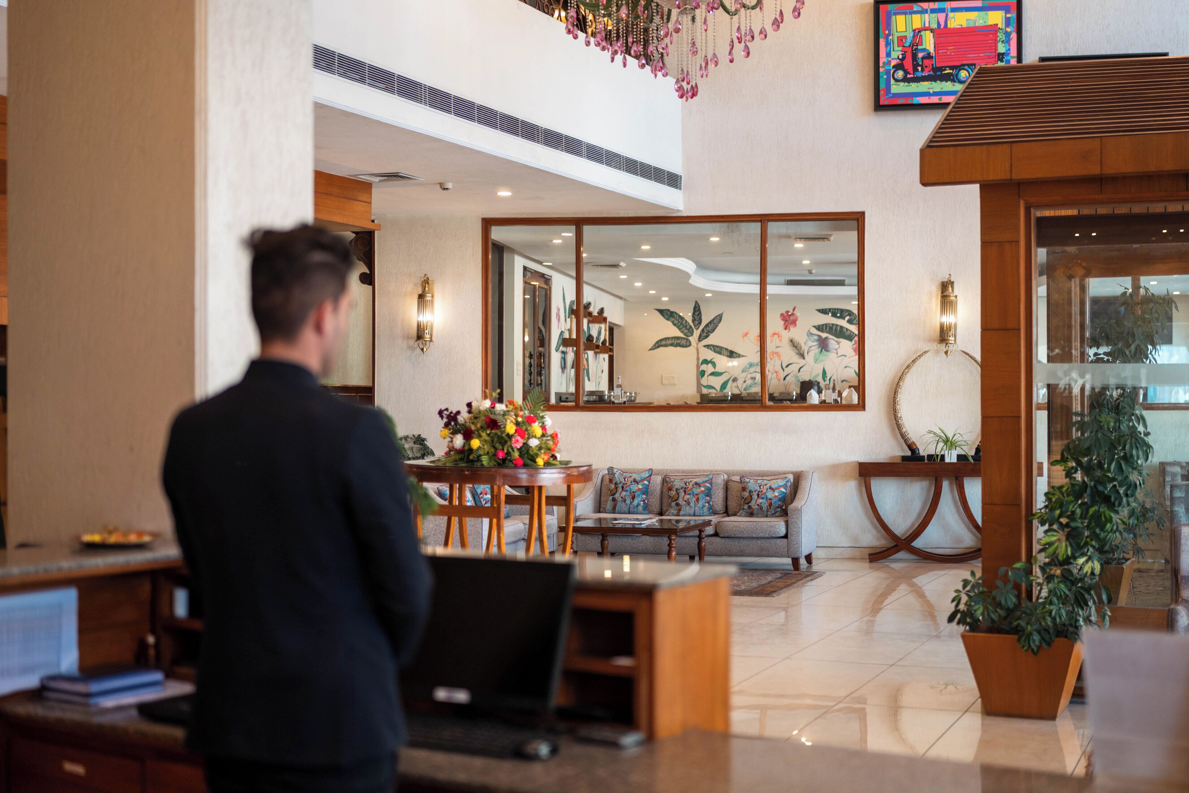 A hotel lobby with a reception desk, seating area, and a large mirror reflecting the interior.