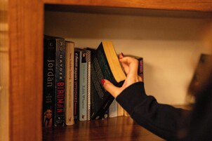 Una mano sostiene un libro de tapa de madera, rodeado de otros libros en una estantería.