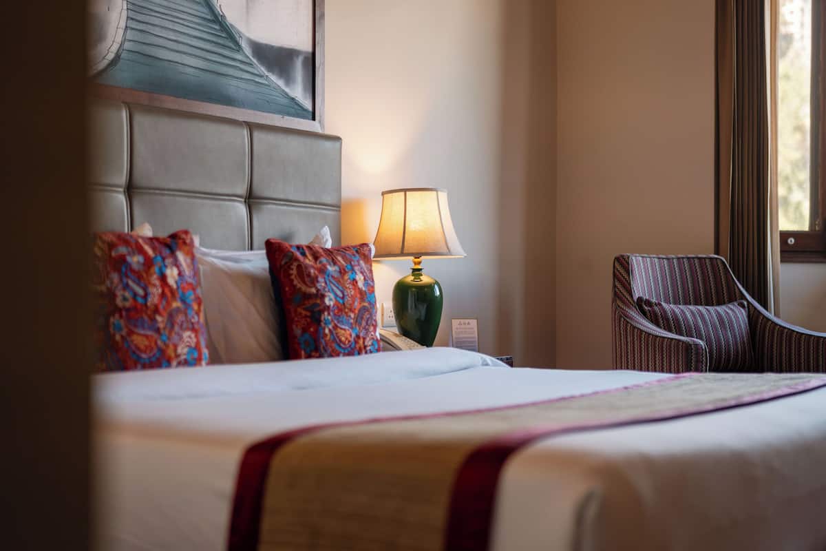 Une chambre d’hôtel avec un lit, une lampe, une chaise et un tableau au mur.