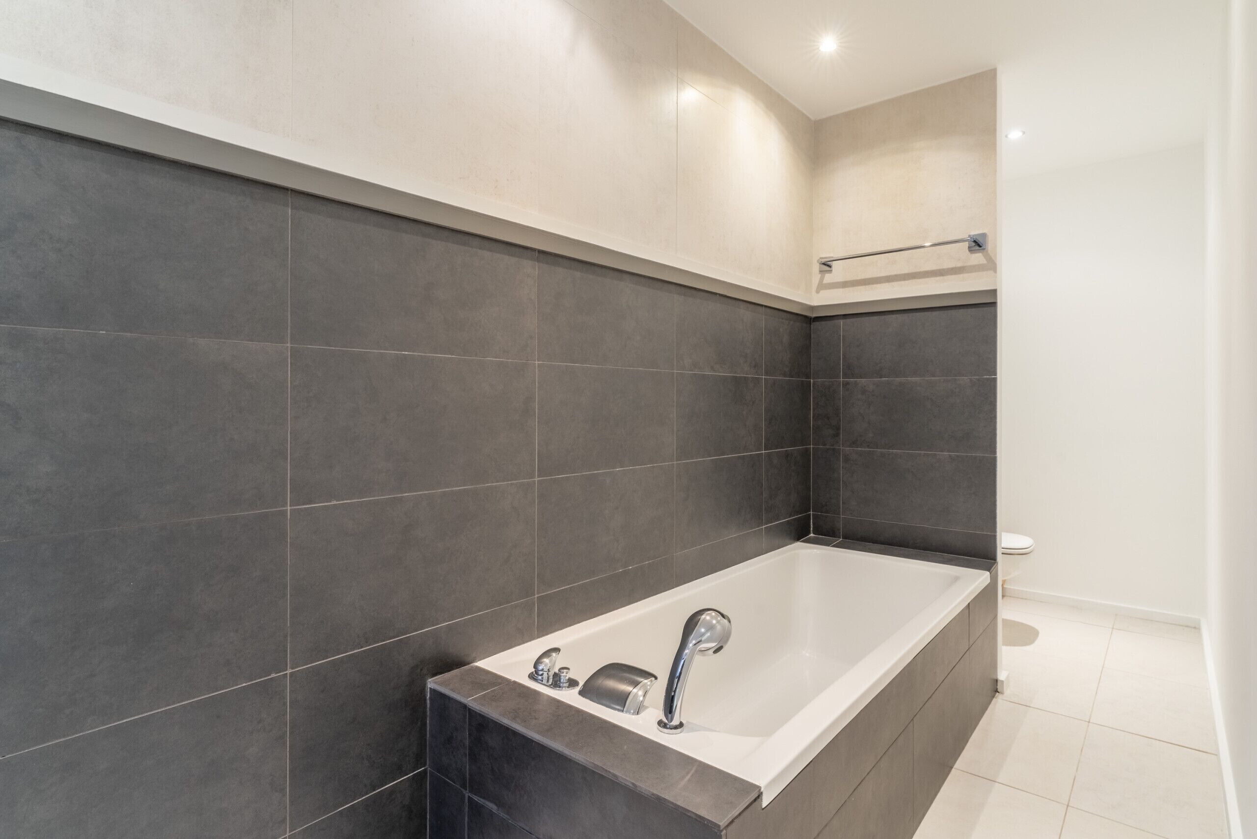 A modern bathroom with a large bathtub, dark tiles, and a white toilet.