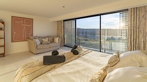 Ett modernt sovrum med en stor säng, en soffa och utsikt över en stadssiluett genom fönster som sträcker sig från golv till tak.