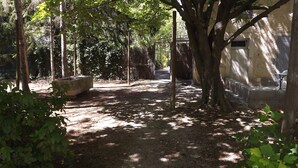 A shaded outdoor area with a stone bench, trees, and a building with a window. - Cottage studio in the countryside (Cavaillon)